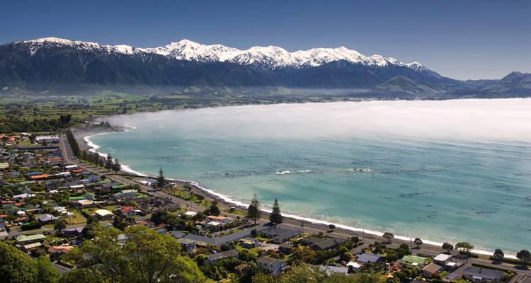 Ville côtière pittoresque avec des montagnes en arrière-plan et une brume marine.