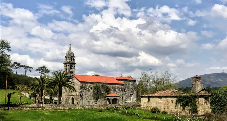 Iglesia de piedra con techo rojo entre vegetación bajo un cielo azul.