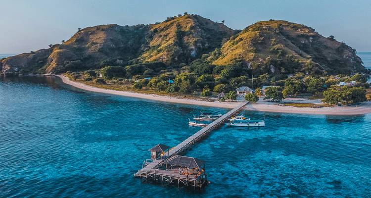 An island with a dock and boats surrounded by clear blue waters.