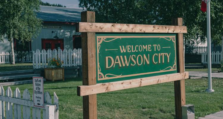 A welcoming sign for Dawson City in a rustic setting.