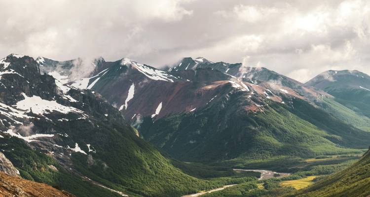 Vasta cordillera montañosa con nieve y valles verdes.