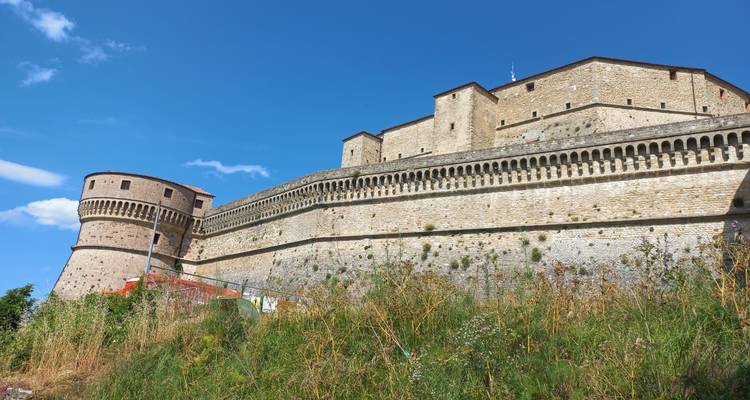 Les murs en pierre d'une forteresse et une tour arrondie se dressent contre un ciel bleu éclatant sur une colline dans la région d'Émilie-Romagne en Italie.