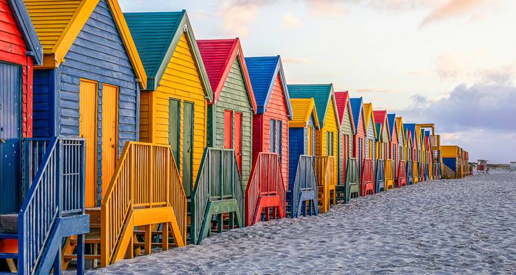 Cabanes de plage colorées alignées sur le sable.