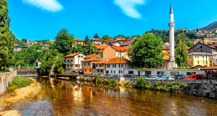 Bâtiments colorés et un minaret au bord d'une rivière à Sarajevo.