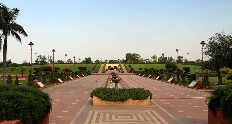 Paseo de jardín simétrico con fuentes y setos bien cuidados que se extienden hacia un montículo cubierto de césped.