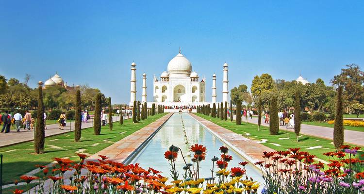Piscina icónica y jardines florales que conducen al brillante Taj Mahal blanco bajo un cielo azul radiante.