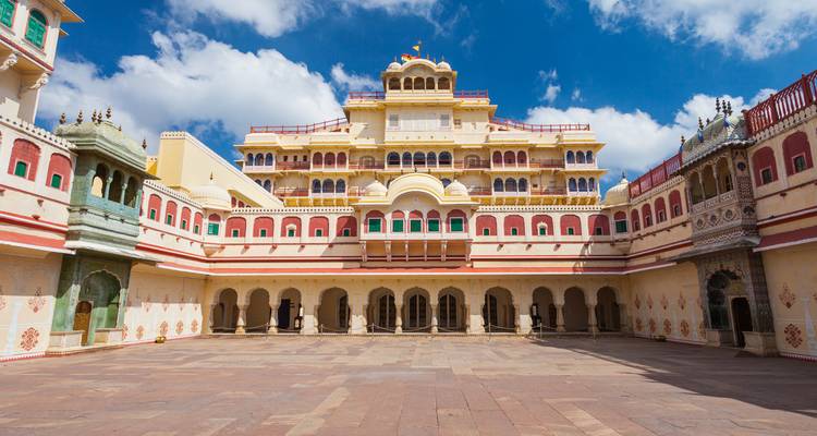 Cour symétrique du Palais de la Ville de Jaipur avec des balcons ornés et une architecture rajpoute colorée sous un ciel bleu éclatant.