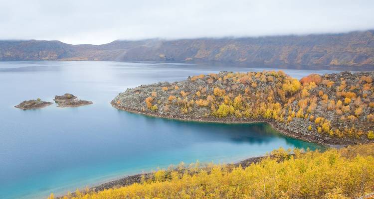 Remote lake with autumn-colored trees on rocky peninsulas beneath a misty ridge.