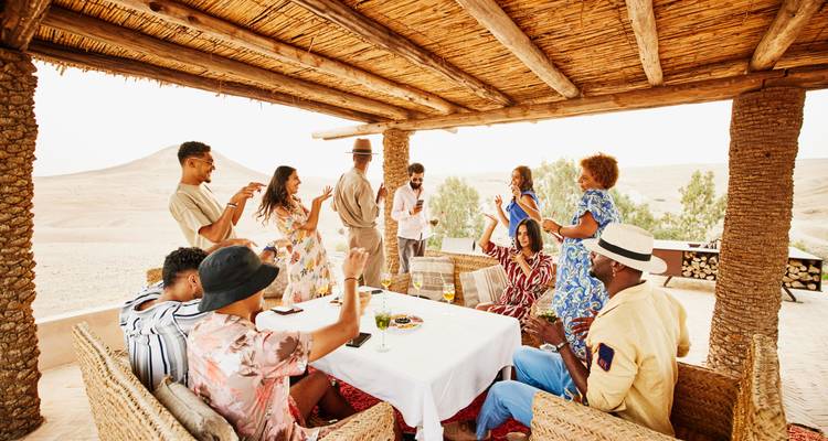 Groep mensen die genieten van een maaltijd en drankjes onder een gevlochten dak.