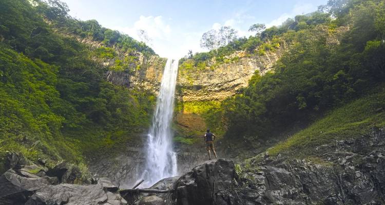 Grande cascade tombant dans une zone rocheuse avec une personne debout à la base.