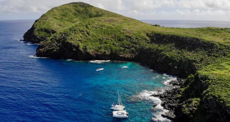 Île escarpée entourée d'une mer bleu profond et de bateaux à l'ancre.