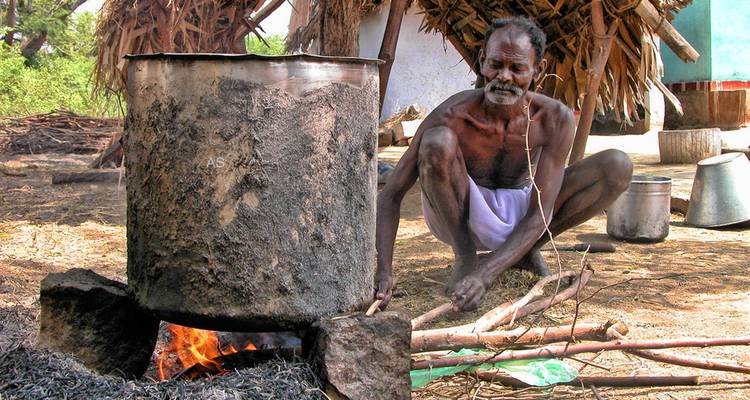 Man tending to a large pot on an open fire outdoors.
