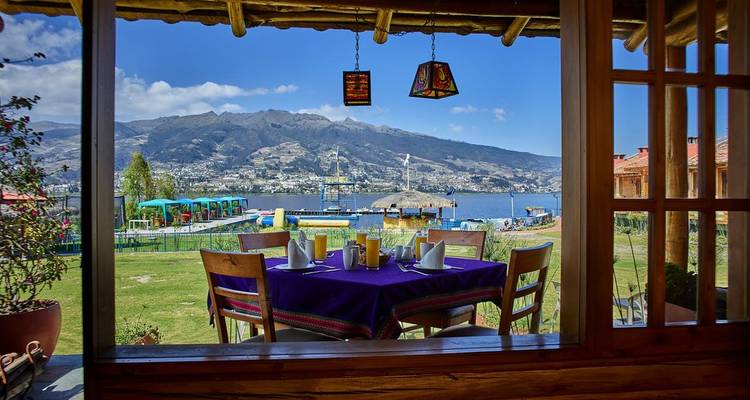 Table à manger dressée pour le petit-déjeuner, avec vue sur un lac et des montagnes par la fenêtre.