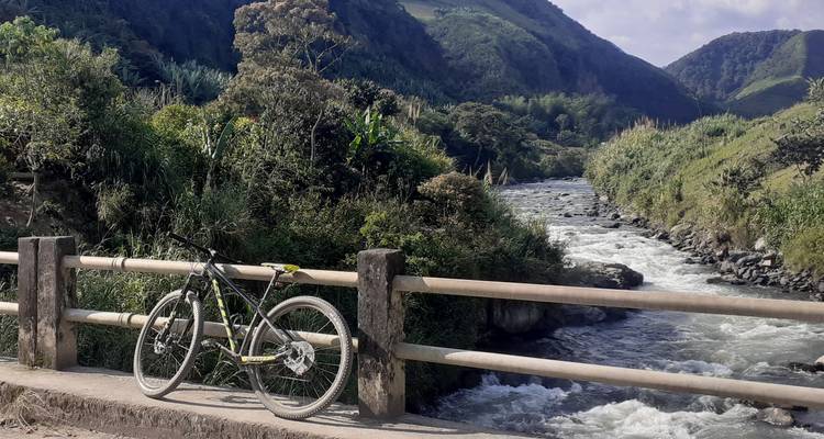 Vélo appuyé contre un pont avec une rivière qui coule et des collines vertes.