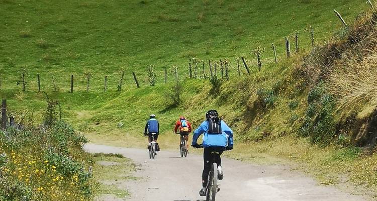 Drie fietsers rijden op een zandpad geflankeerd door groene heuvels en hekken.