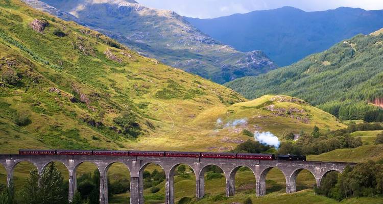 Glenfinnan Viaduct with steam train passing through lush green hills.