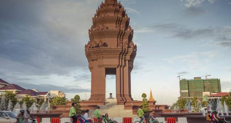 A monument with intricate details surrounded by fountains and people riding bicycles.