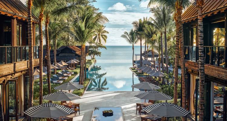 Complexe de luxe avec piscine au milieu des palmiers surplombant l'océan.