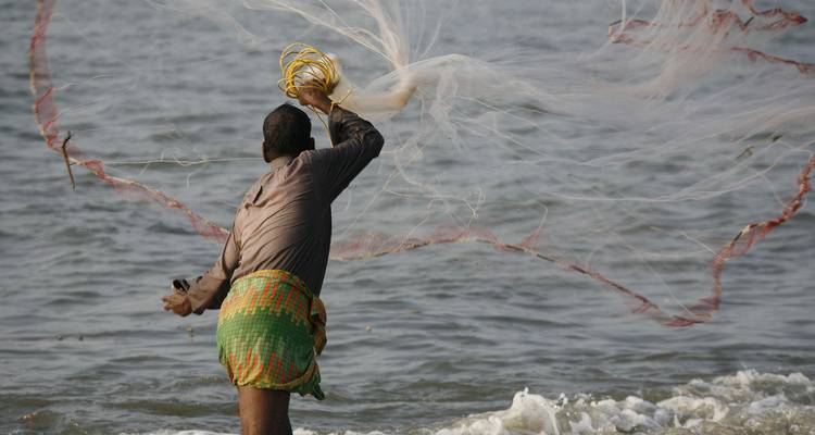Homme lançant un filet de pêche dans l'eau.