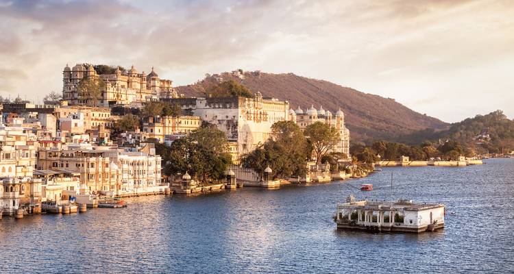 Stadsgezicht van Udaipur met gebouwen naast een meer bij zonsondergang.