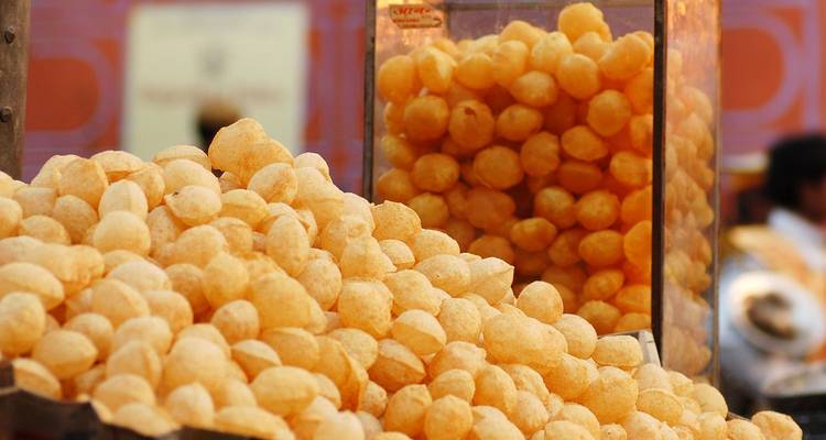 Heap of crispy pani puri shells on a street vendor’s cart with colourful blurry background.