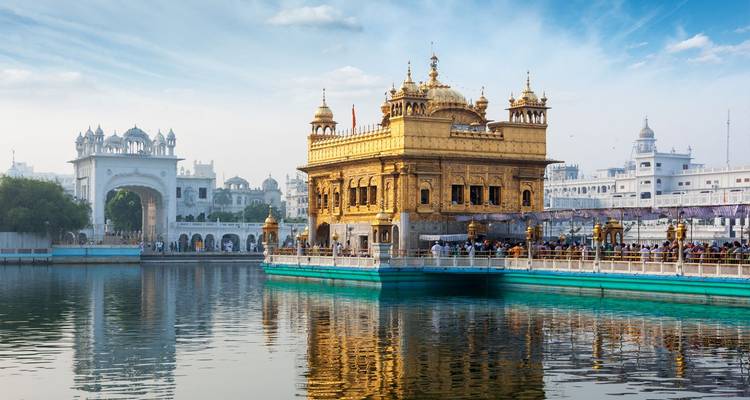 Golden Temple glows above its sacred pool with white archway and blue-tinged sky reflecting in the water.
