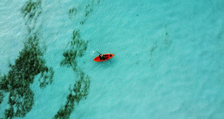 Una persona navegando en kayak sobre agua turquesa cristalina.