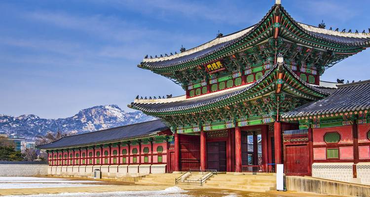 Ornate red and green Heungnyemun Gate of Gyeongbokgung with snowy mountains in background.