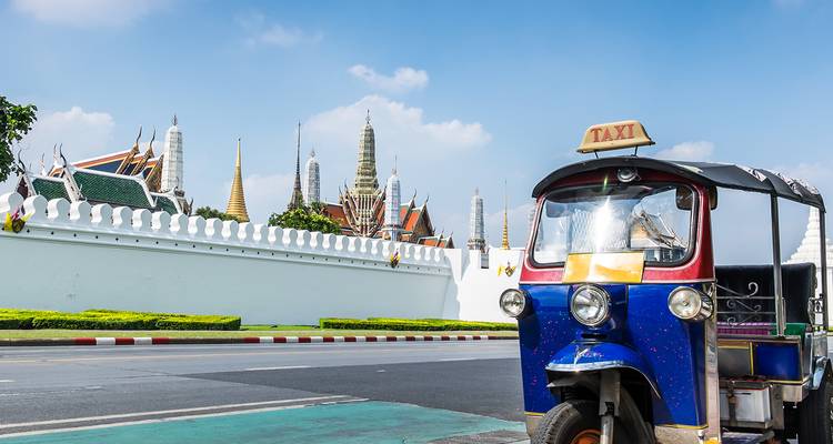 Taxi tuk-tuk azul estacionado frente a los muros blancos del Gran Palacio de Bangkok.