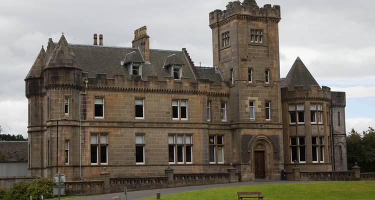 Vieux château de pierre, avec une pelouse herbeuse devant.