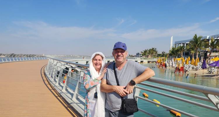 Couple posing on a boardwalk near water with cityscape.