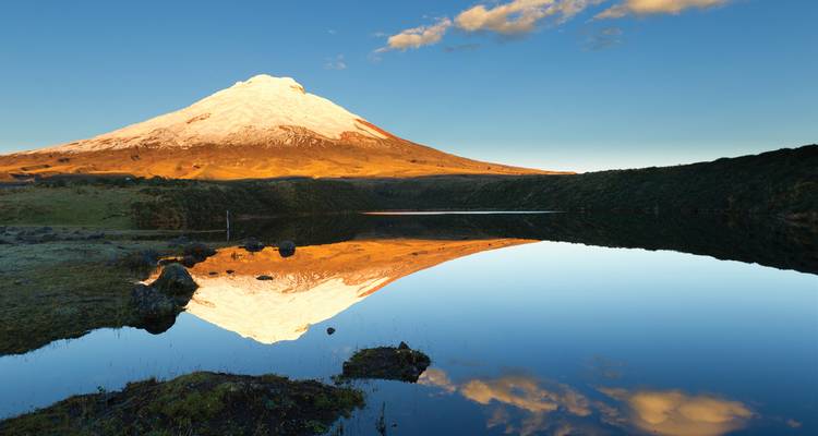 Snow-capped mountain peak reflecting in a still lake at sunset.