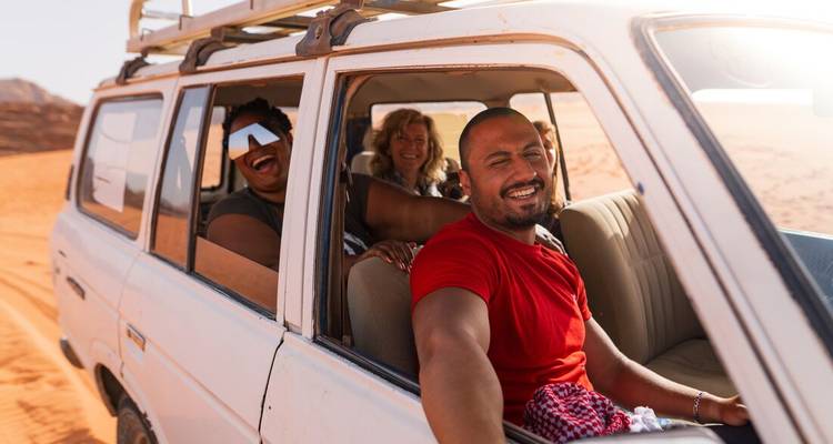 Groupe de personnes souriantes dans un véhicule tout-terrain lors d'un safari dans le désert.