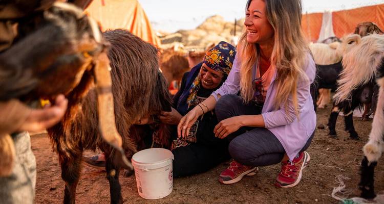 Une femme locale apprenant à un touriste comment traire une chèvre.