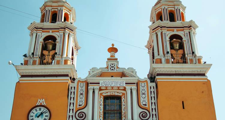 Bright orange colonial church facade with two ornate bell towers against a clear blue sky.
