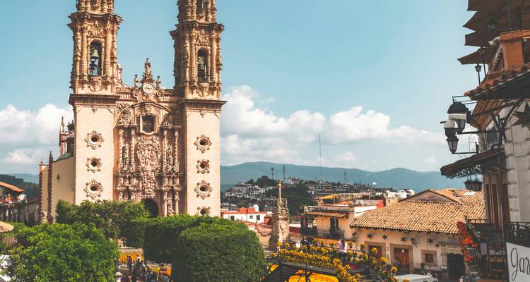 Panoramic view of Taxco’s historic center with the ornate Santa Prisca Cathedral rising above whitewashed houses and distant mountains.