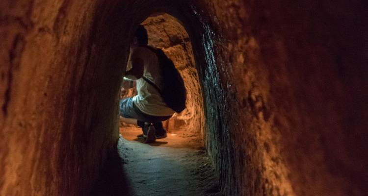 Person inside a dark tunnel with rough walls and narrow passage.