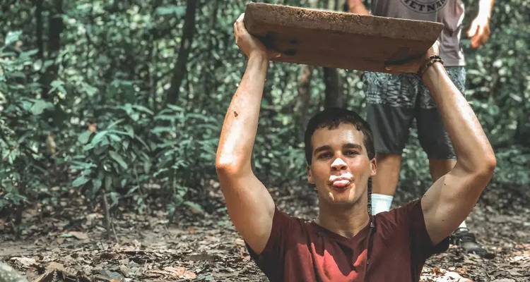 Man playfully holding a piece of wood above his head in a forest setting.