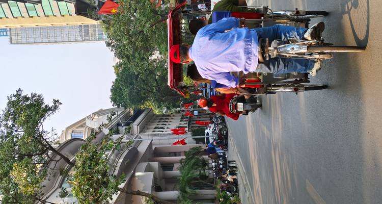 Cyclo drivers pedalling through a lively city street adorned with red flags