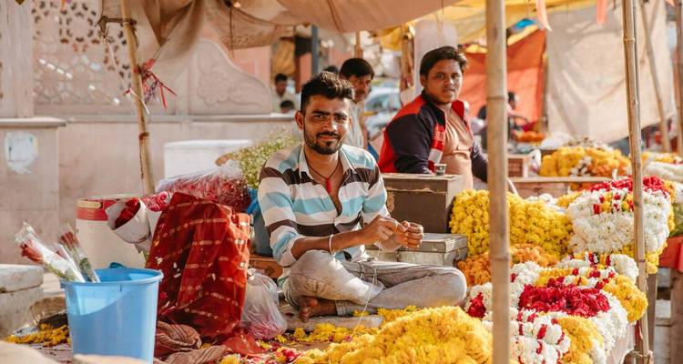 Hombres sentados entre flores coloridas en un ambiente de mercado.