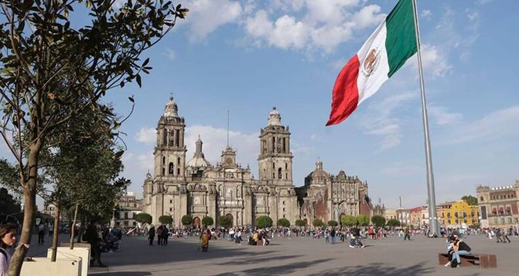 De Metropolitan Cathedral van Mexico City kijkt uit over het grote Zócalo-plein waar mensen zich verzamelen onder een gigantische vlag