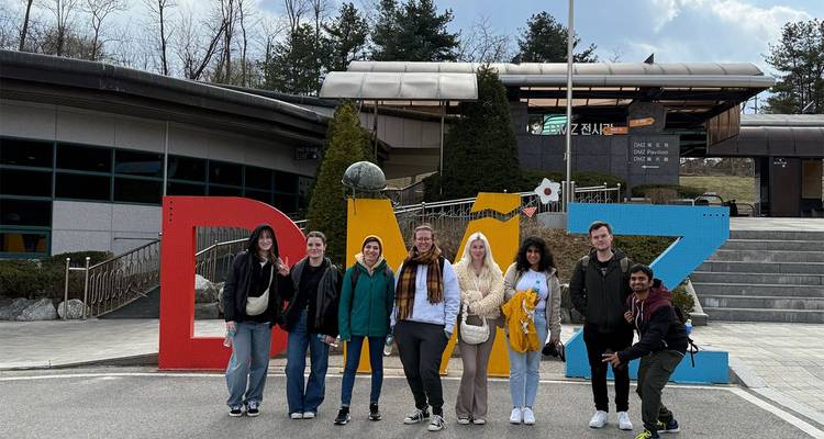 Tour group poses in front of large colourful DMZ letters outside the demilitarized zone visitor centre.