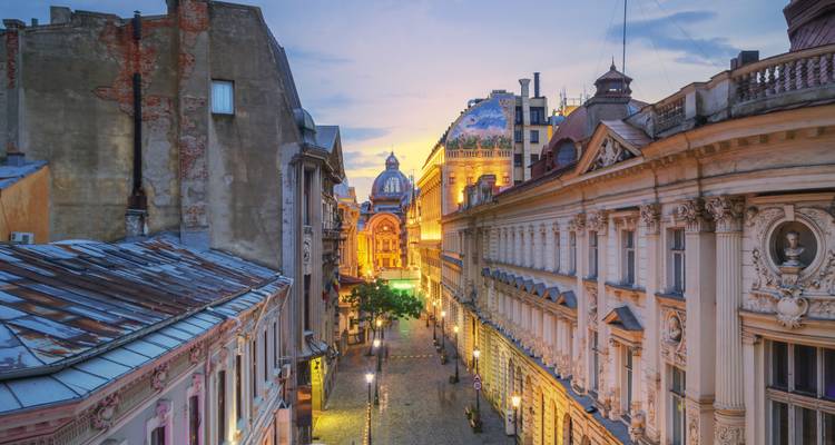 Vue au crépuscule d'une rue piétonne étroite donnant sur le Palais CEC illuminé à Bucarest.