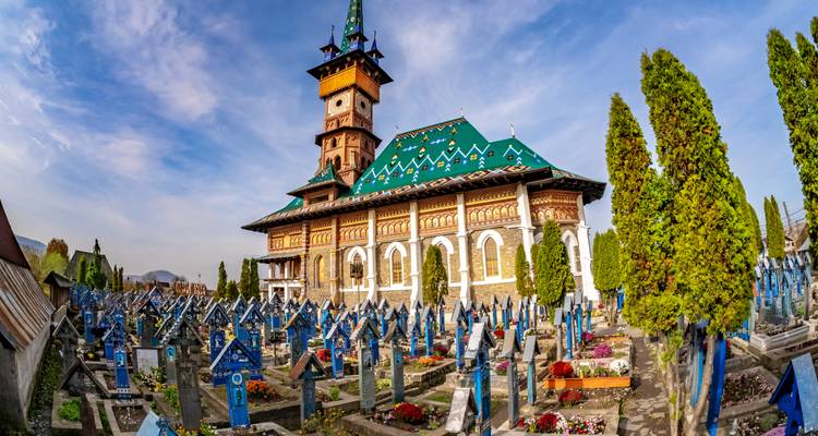 Les pierres tombales colorées du Cimetière Joyeux avec une église en bois en Maramureș.