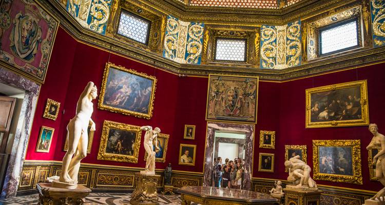 Salle de galerie aux murs rouge luxueux avec des panneaux de plafond dorés et des sculptures classiques entourant les touristes.