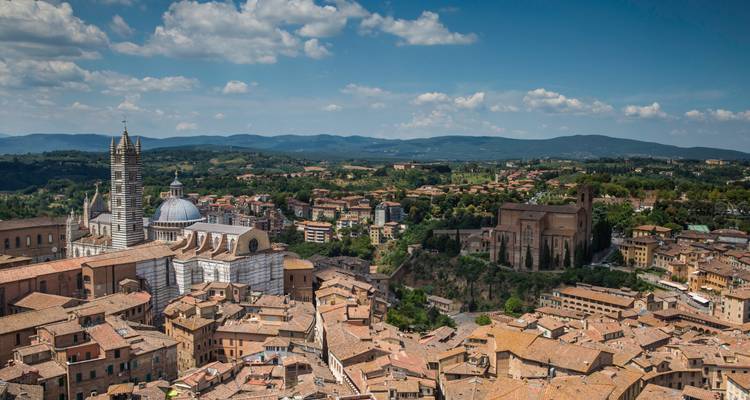 Panorama aérien d'une ville historique avec des dômes de cathédrale, une façade en marbre rayé et des collines ondulantes au-delà.