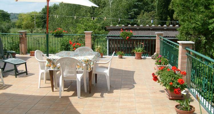 Terrasse carrelée simple avec des chaises et une table en plastique donnant sur la campagne verdoyante.