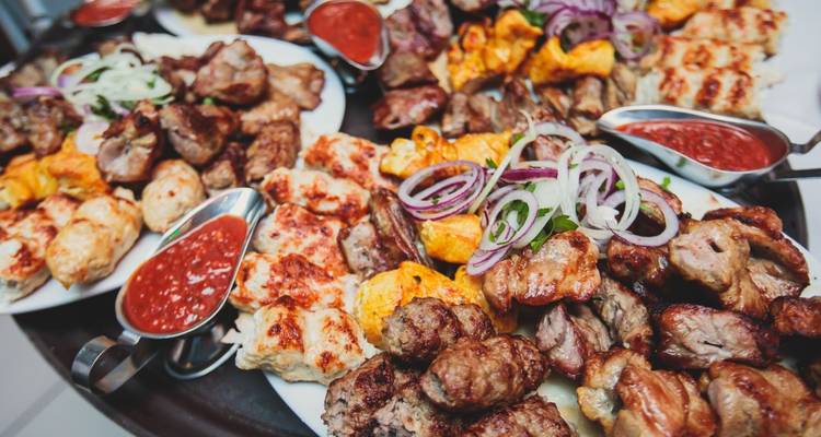 Verschiedene gegrillte Fleischsorten auf Tellern mit Soßen.