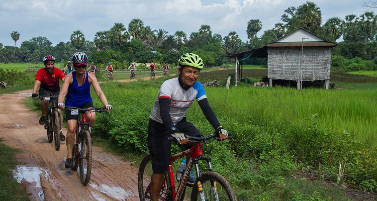Cyclists biking on a dirt path alongside tropical foliage.