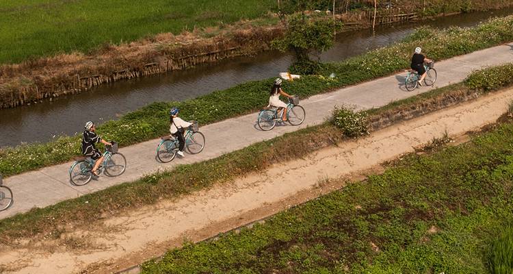Cyclists riding along a canal on a narrow path.